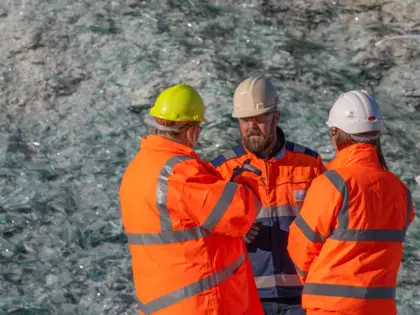 Three people standing in front of glass cullet in high vis jackets